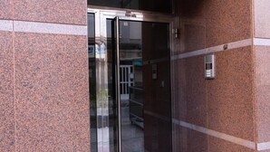 Entrada de un edificio con puerta de vidrio, una reja metálica y un pequeño letrero en la pared.