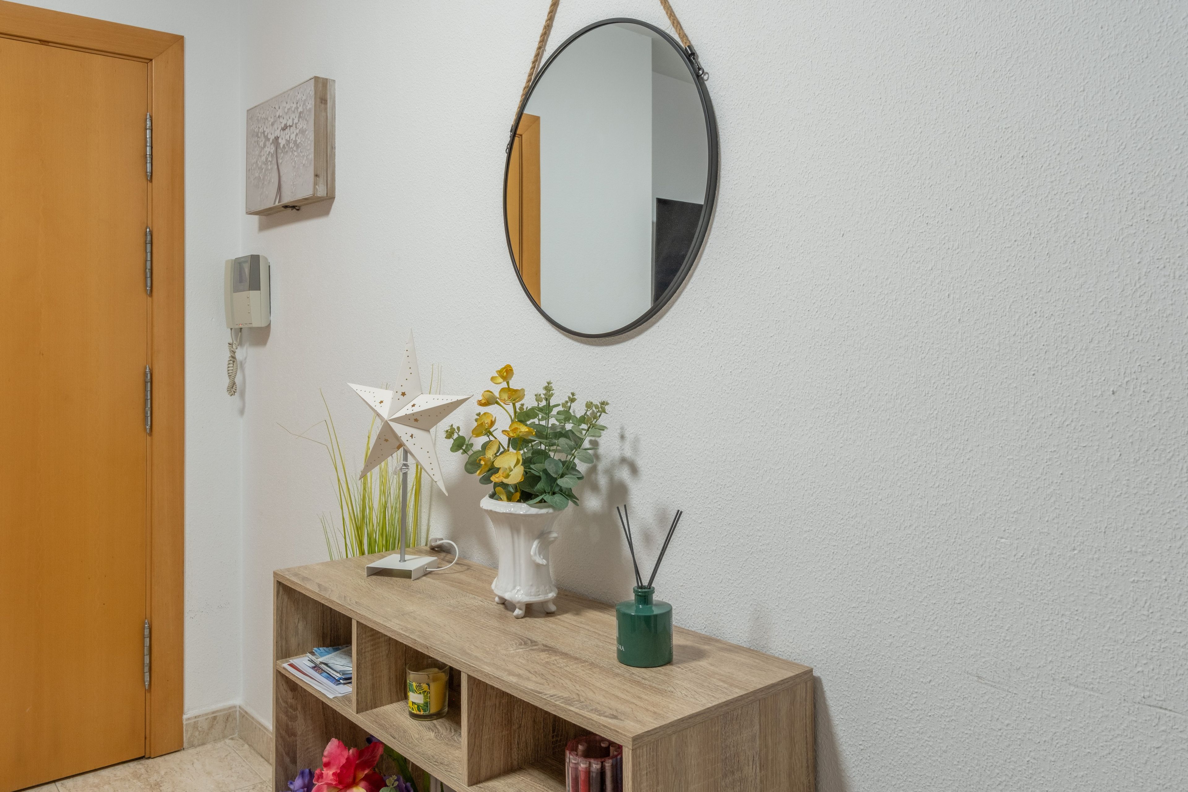 A wooden console table with a mirror, a vase with yellow flowers, a small plant, and a candle.