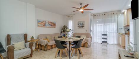 A modern living room with a dining area, a ceiling fan, and a kitchen with a TV.