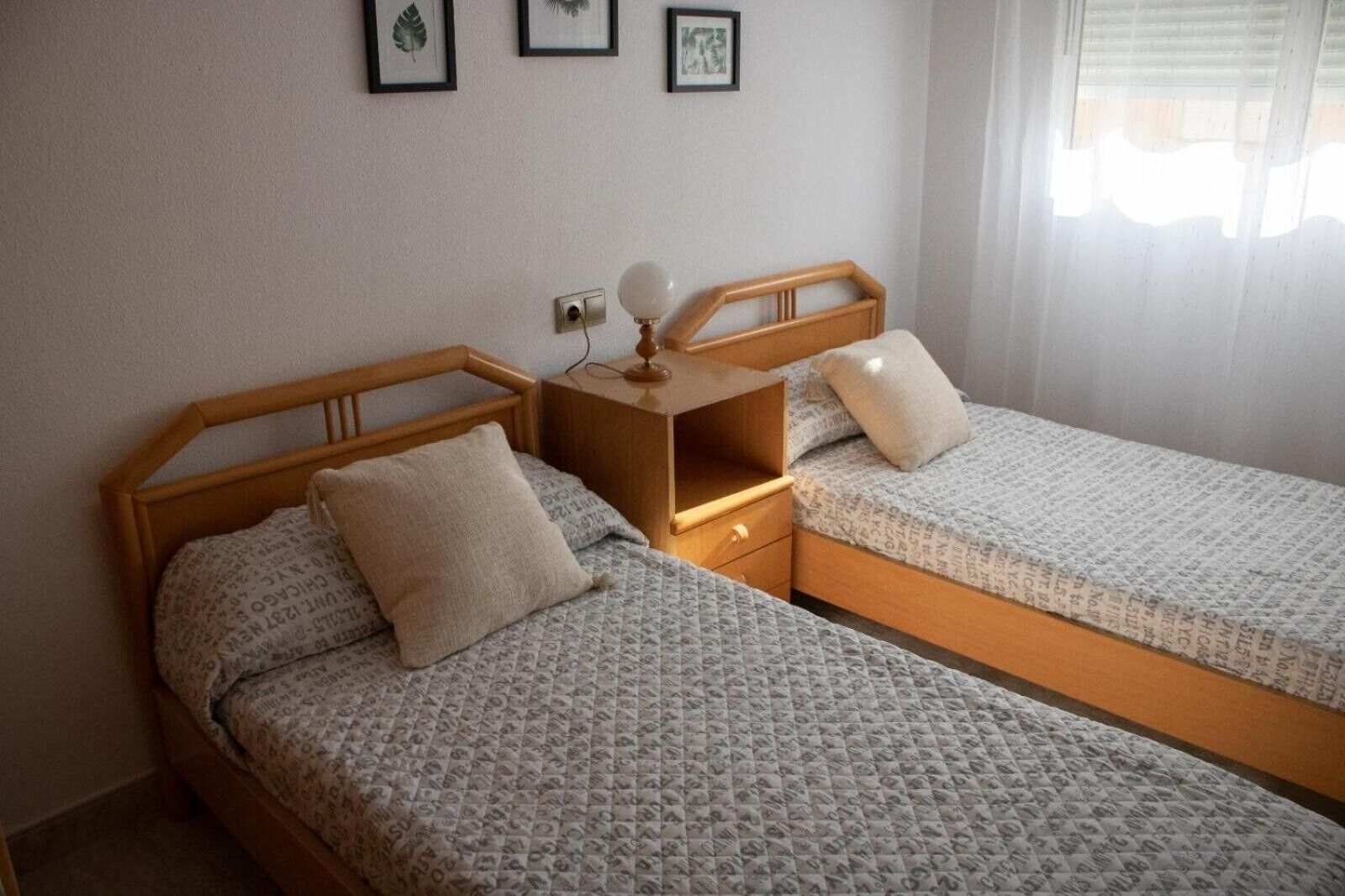 Una habitación con dos camas de madera, una mesita de noche con lámpara y cuadros en la pared.