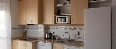 Una cocina con armarios de madera, microondas, fregadero, lavavajillas y lavadora.