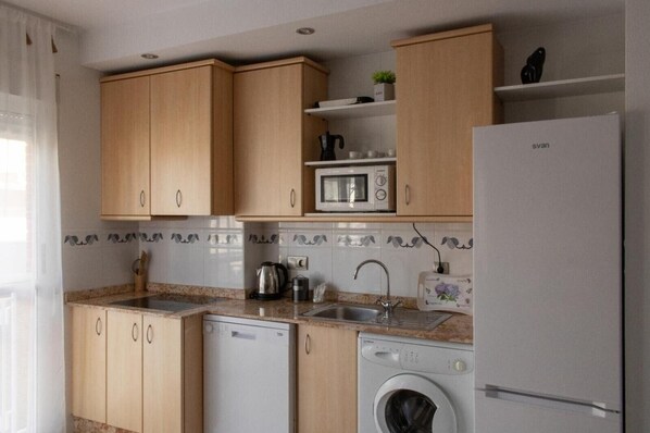 A kitchen with wooden cabinets, a microwave, a sink, a dishwasher, and a washing machine.