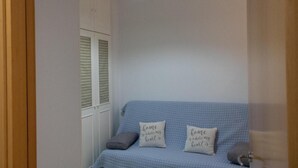 Habitación con sofá azul, dos almohadas con texto, un armario blanco y una lámpara colgante.