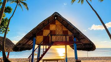 Eine Strandhütte mit Reetdach, Holzbauweise und einer Sitzbank.