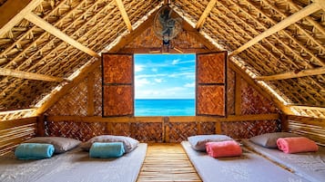 Una habitación con techo de paja, un ventanal con vistas al mar y dos camas con toallas.