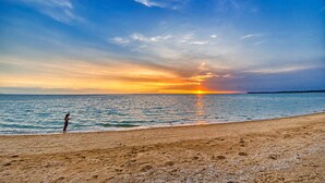 Una playa con un atardecer, cielo despejado y mar tranquilo.