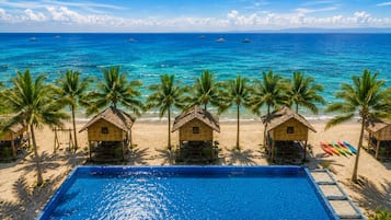 Un hotel frente al mar con piscina, palmeras y cabañas de playa.