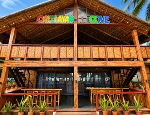 Ein zweistöckiges Holzhaus mit einem Strohdach, mit dem Schriftzug 'CALTAYAN COVE'.