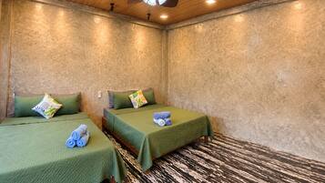 A room with two beds, each with a green bedspread and a pillow, a ceiling fan, and a textured wall.