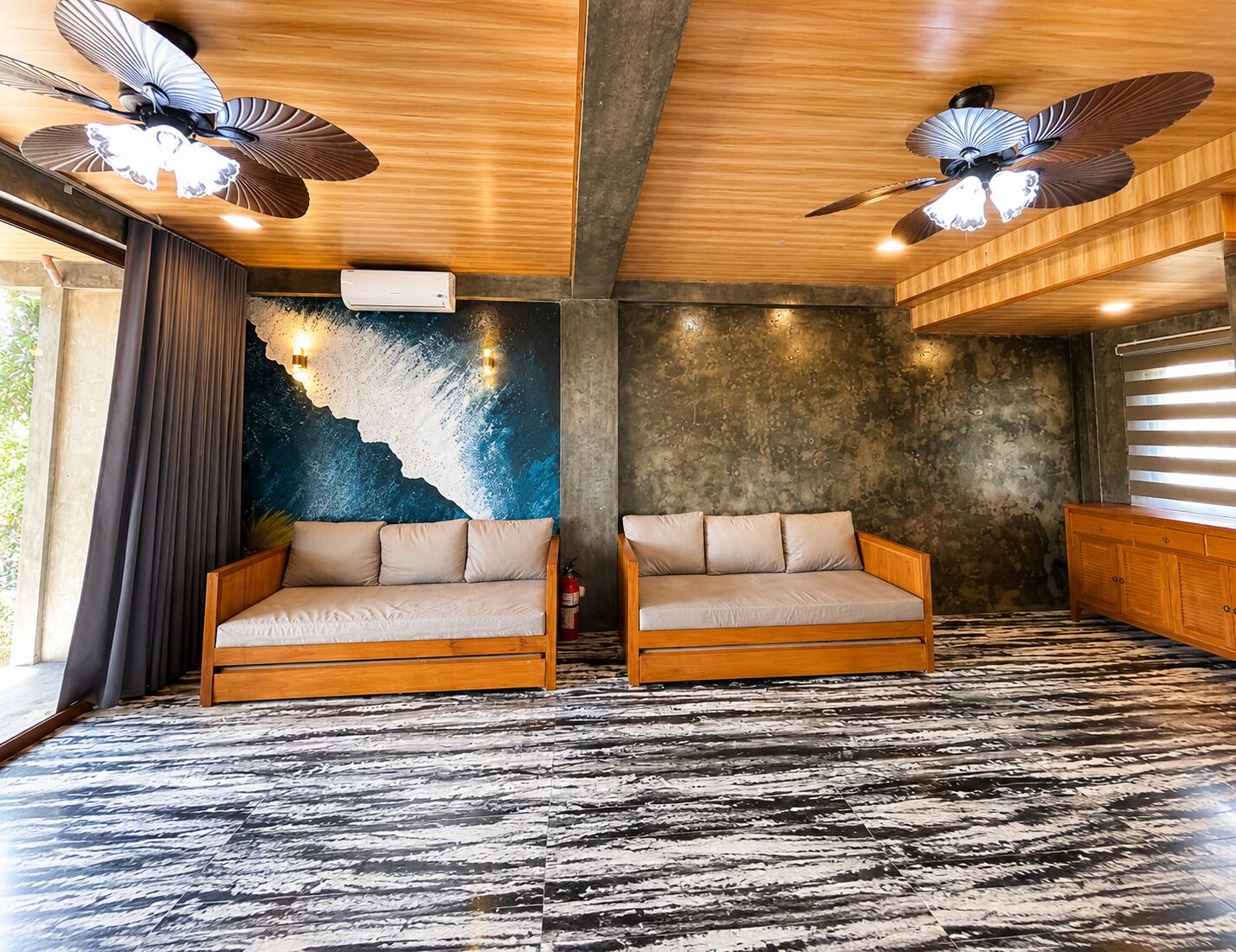 Quarto com dois sofás, um ventilador de teto, parede texturizada e piso estampado.