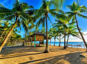 A beach with palm trees, a wooden hut, and a sandy path. - Calilayan Cove Beach Resort (Unisan)
