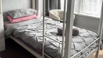 Un lit superposé avec un matelas et des oreillers gris, une petite chaise et une fenêtre avec des rideaux.