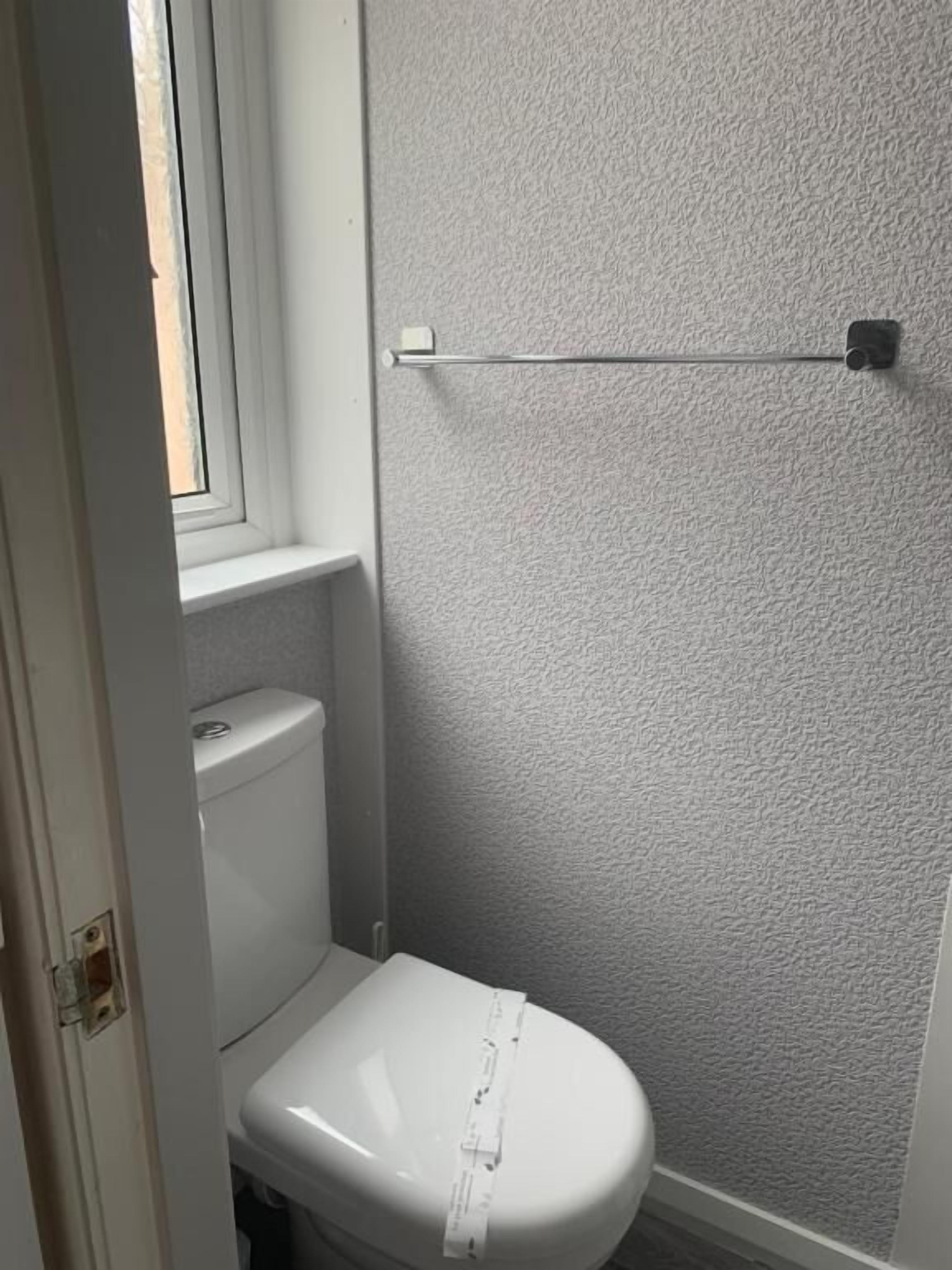 Un baño pequeño con inodoro blanco, ventana y pared texturizada.