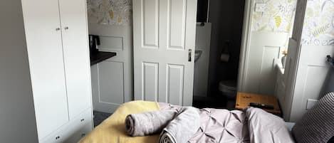 Een slaapkamer met een bed, een kledingkast, een zichtbare badkamer door een geopende deur, en een tafeltje met een afstandsbediening.