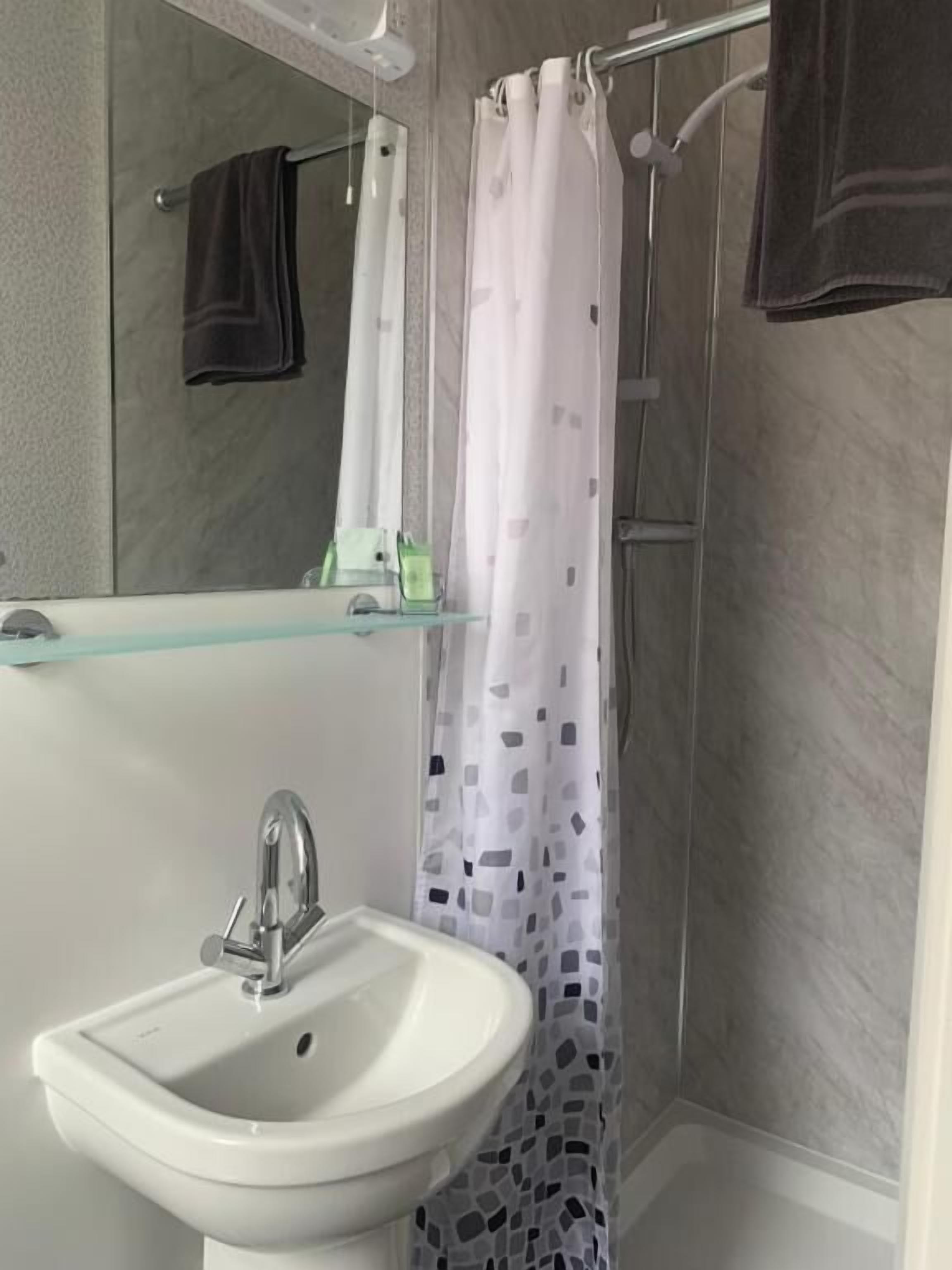 Un baño con repisa de vidrio, lavamanos blanco y cortina de ducha.