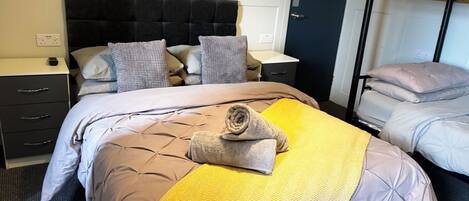 A hotel room with a bed, a nightstand, a dresser, a bunk bed, and a wall-mounted light fixture.
