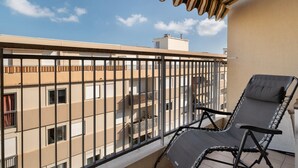 A balcony with a black metal railing, a black lounge chair, and a striped awning.