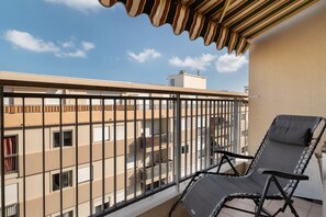 A balcony with a black metal railing, a black lounge chair, and a striped awning.