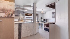 A modern kitchen with a central island, a dining area with a white table and chairs, and a living area with a sofa and a TV.