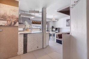 A modern kitchen with a central island, a dining area with a white table and chairs, and a living area with a sofa and a TV.