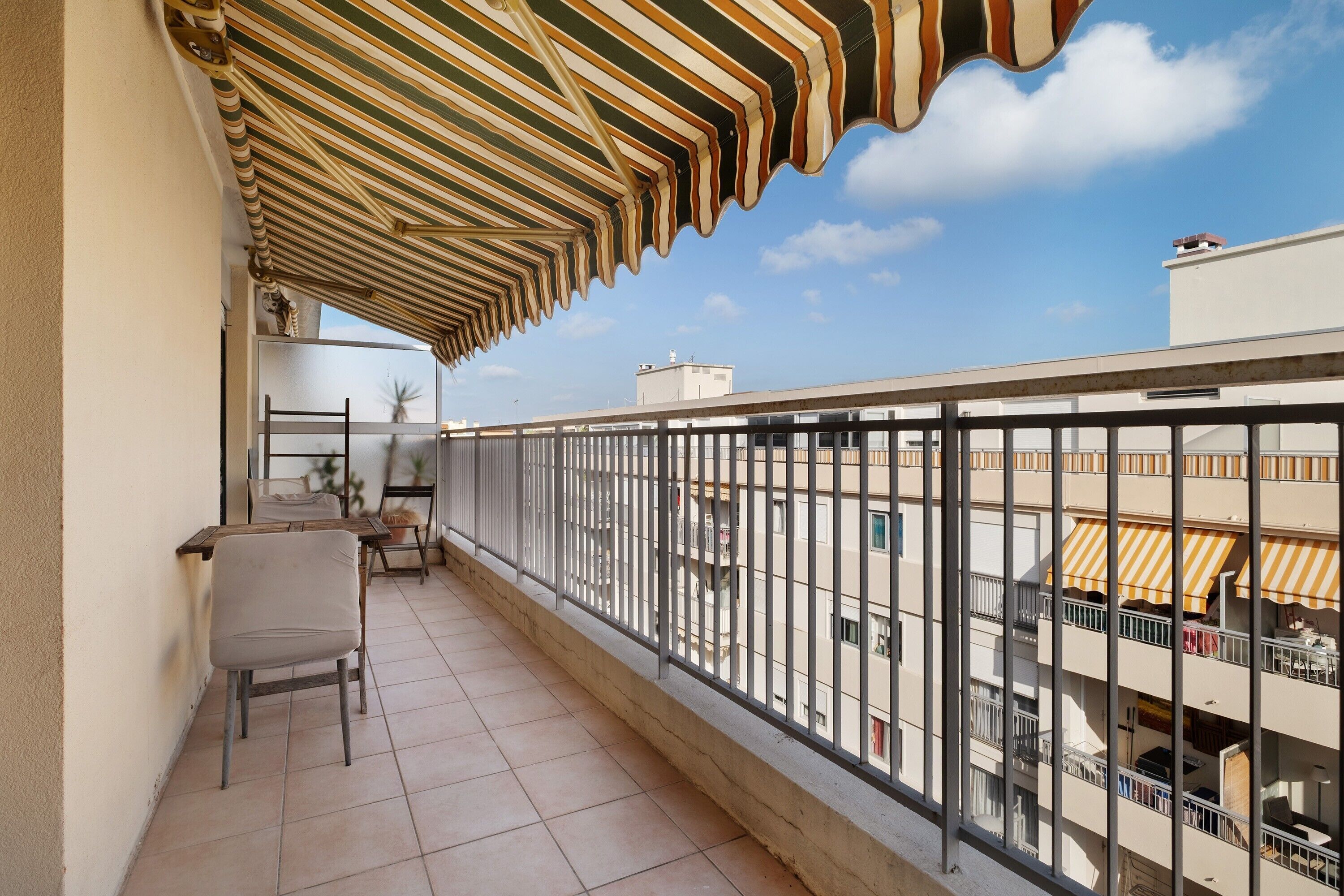 Un balcon avec un auvent à rayures, une chaise et une table.