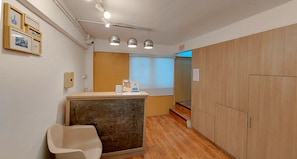 A hotel room with a wooden floor, a reception desk, a white chair, and a wooden wardrobe. - Ze Residence Bang Aor Station  (Bangkok)