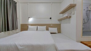 Hotelkamer met een enkel bed, een nachtkastje, een plank met handdoeken en een douche.