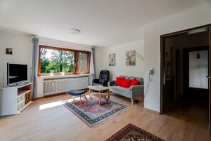 Un salon moderne avec un téléviseur, des sièges, un radiateur et une fenêtre donnant sur un espace verdoyant.