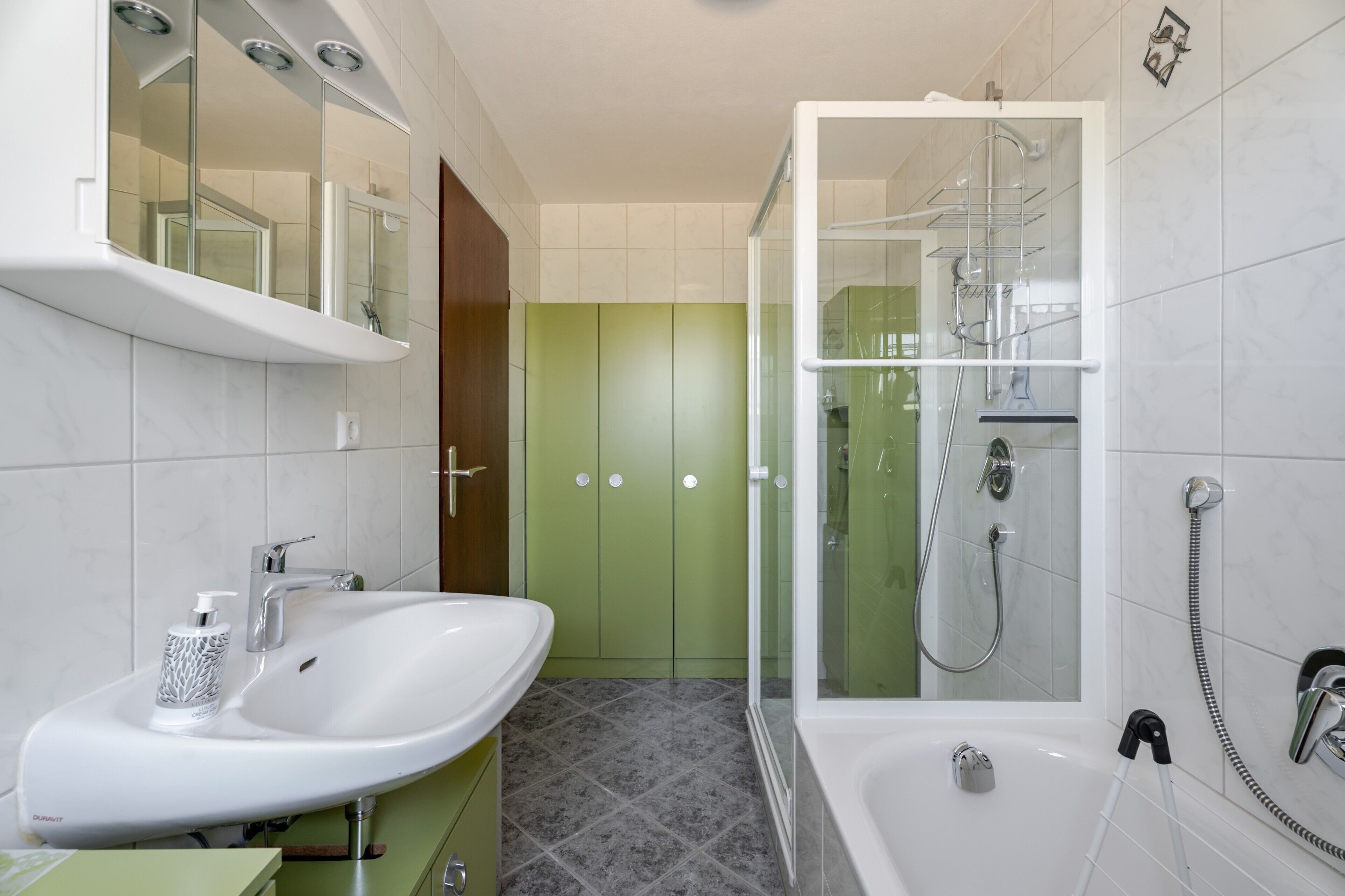 Ein modernes Badezimmer mit einem weißen Waschbecken, einer gläsernen Dusche und einer grünen Tür.