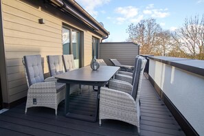 An outdoor deck with a dining table and chairs, a small table lamp, and a view of trees and sky. - Baltic Sea Horizon – Penthouse. Sauna. Roof terrace. (Kellenhusen)