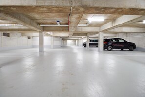 An underground parking garage with concrete pillars, a black SUV, and a white car parked. - Baltic Sea Horizon – Penthouse. Sauna. Roof terrace. (Kellenhusen)