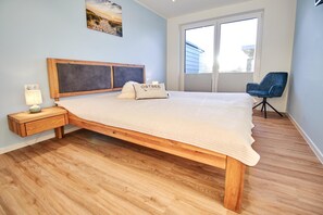A bedroom with a wooden bed, a nightstand, a lamp, a chair, and a window with blinds. - Baltic Sea Horizon – Penthouse. Sauna. Roof terrace. (Kellenhusen)