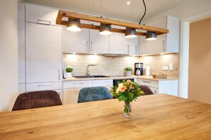 A modern kitchen with white cabinets, a wooden countertop, and a dining table with a vase of flowers. - Baltic Sea Horizon – Penthouse. Sauna. Roof terrace. (Kellenhusen)