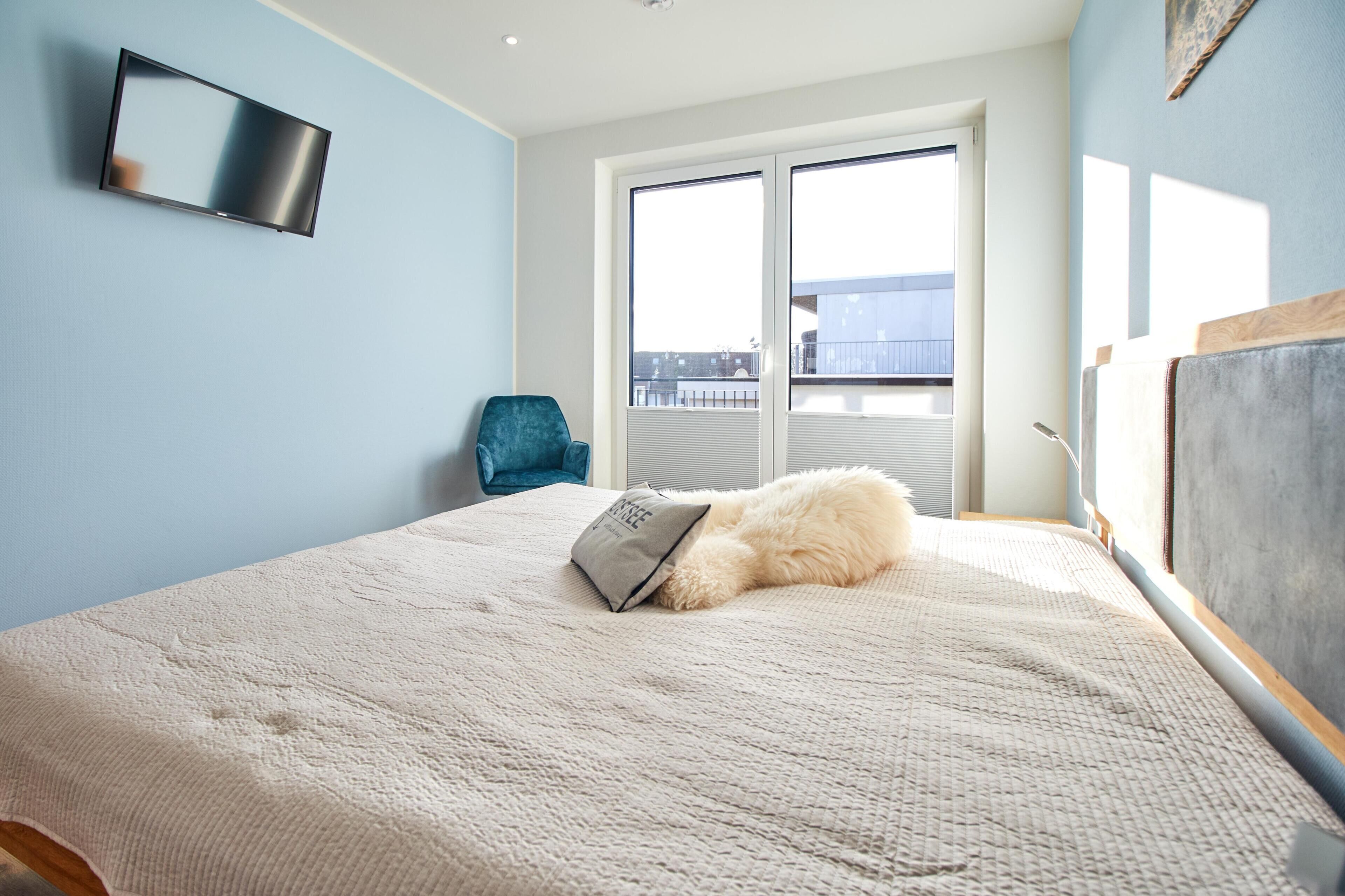 Ein Schlafzimmer mit Bett, Sessel, Fernseher und Blick ins Freie.