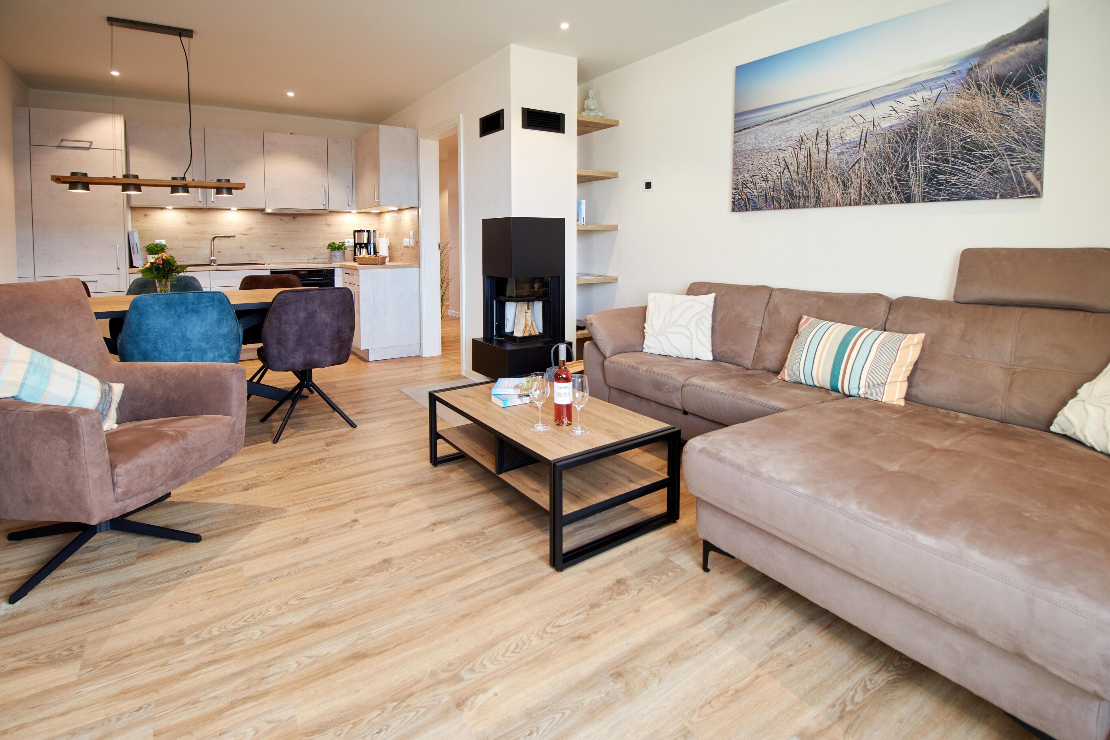 A modern living room with a sofa, armchairs, a coffee table, and a dining area with a kitchen in the background.