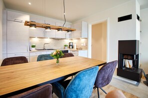 A modern kitchen with a wooden dining table, blue chairs, and a built-in fireplace. - Baltic Sea Horizon – Penthouse. Sauna. Roof terrace. (Kellenhusen)