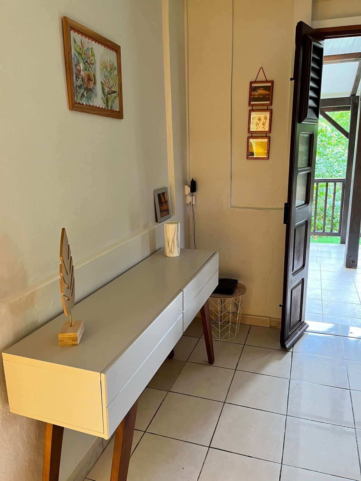 A room with a long, white console table, a small decorative item on the table, a framed picture on the wall, and a door leading outside.