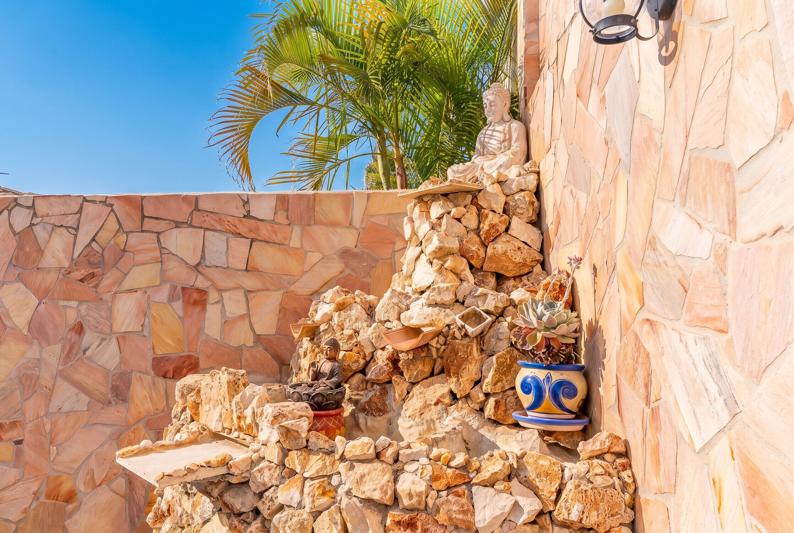 A stone wall with a Buddha statue and potted plants.