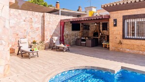 Ett område vid poolen med en stenmur, två solstolar, en grill och en liten pool.
