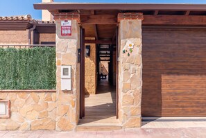 A stone entrance with a wooden door, a sign indicating a 24-hour alarm service, and a flower-shaped plaque on the wall. - Cubo's Buddha Harmony House / Private pool / Air conditioning / BBQ / Free Wi-Fi (Pizarra)