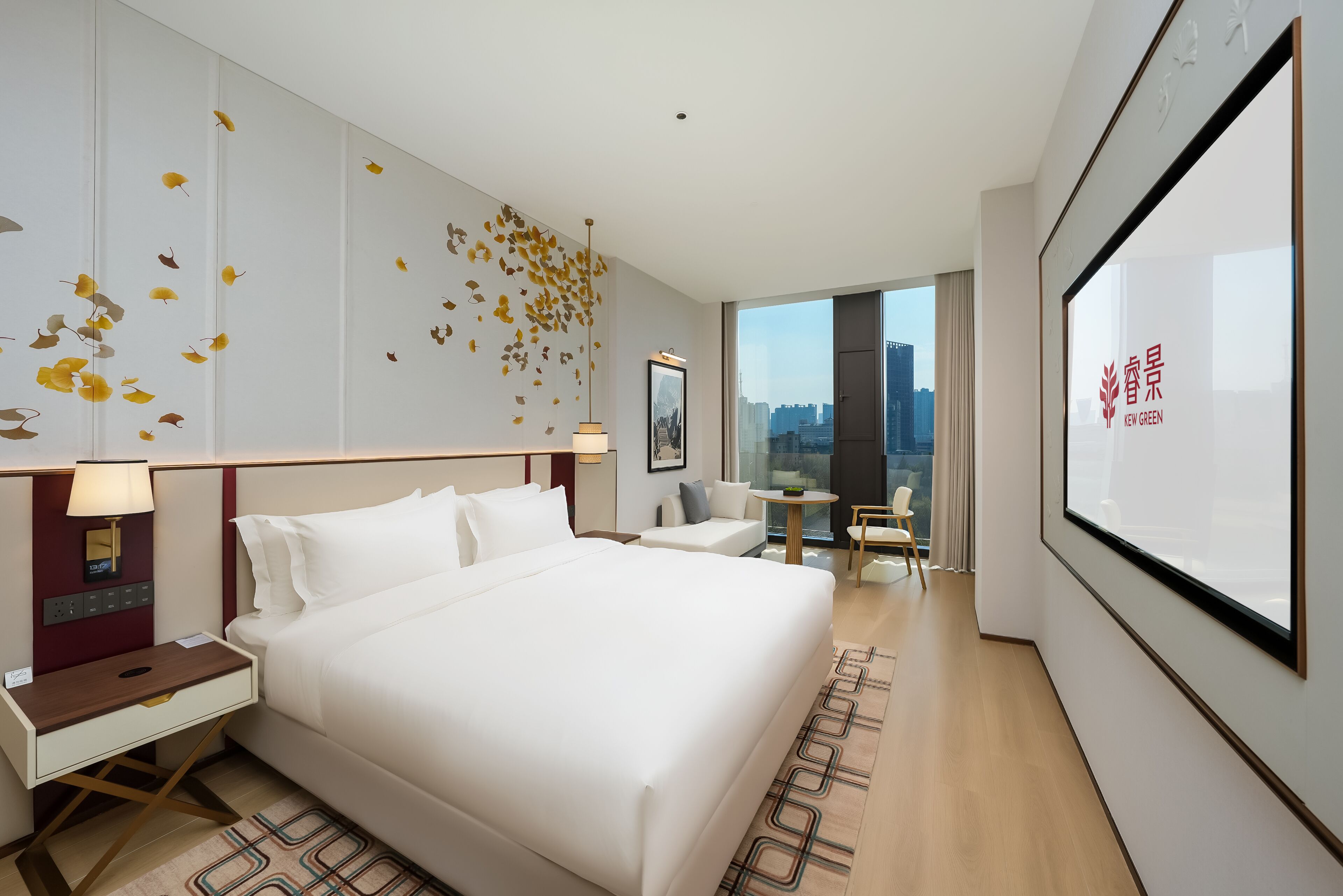 Habitación de hotel moderna con una cama grande, mesitas de noche, un escritorio y vistas a la ciudad a través de un ventanal.