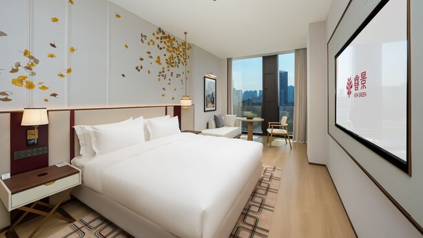 A modern hotel room with a large bed, bedside tables, a desk, and a view of the city through a large window. - Kew Green Chengdu  Hotel (Chengdu)