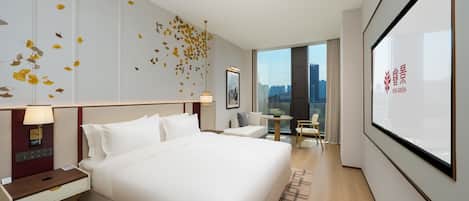 A modern hotel room with a large bed, bedside tables, a desk, and a view of the city through a large window.
