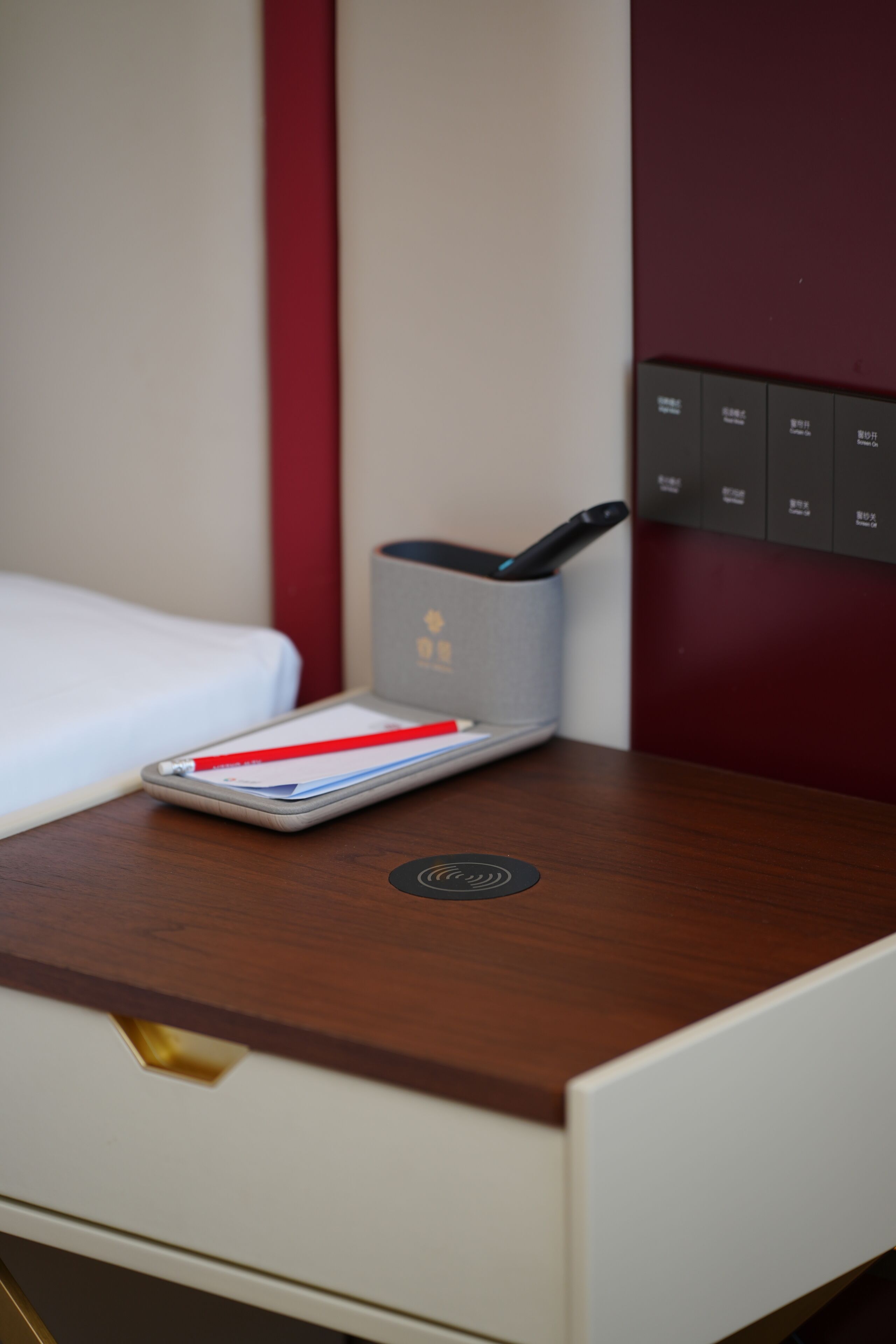 Habitación de hotel con mesita de noche de madera, un cajón y una pequeña mesa con control remoto y bolígrafo.