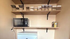 Uma cozinha compacta com micro-ondas, um refrigerador pequeno e prateleiras acima com potes e recipientes.