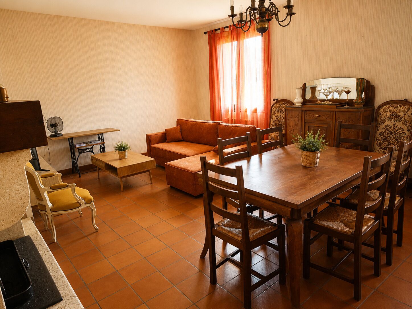 Ein Essbereich mit Holztisch und -stühlen, einer Couch, einem Ventilator und einer Vitrine mit Dekoration.