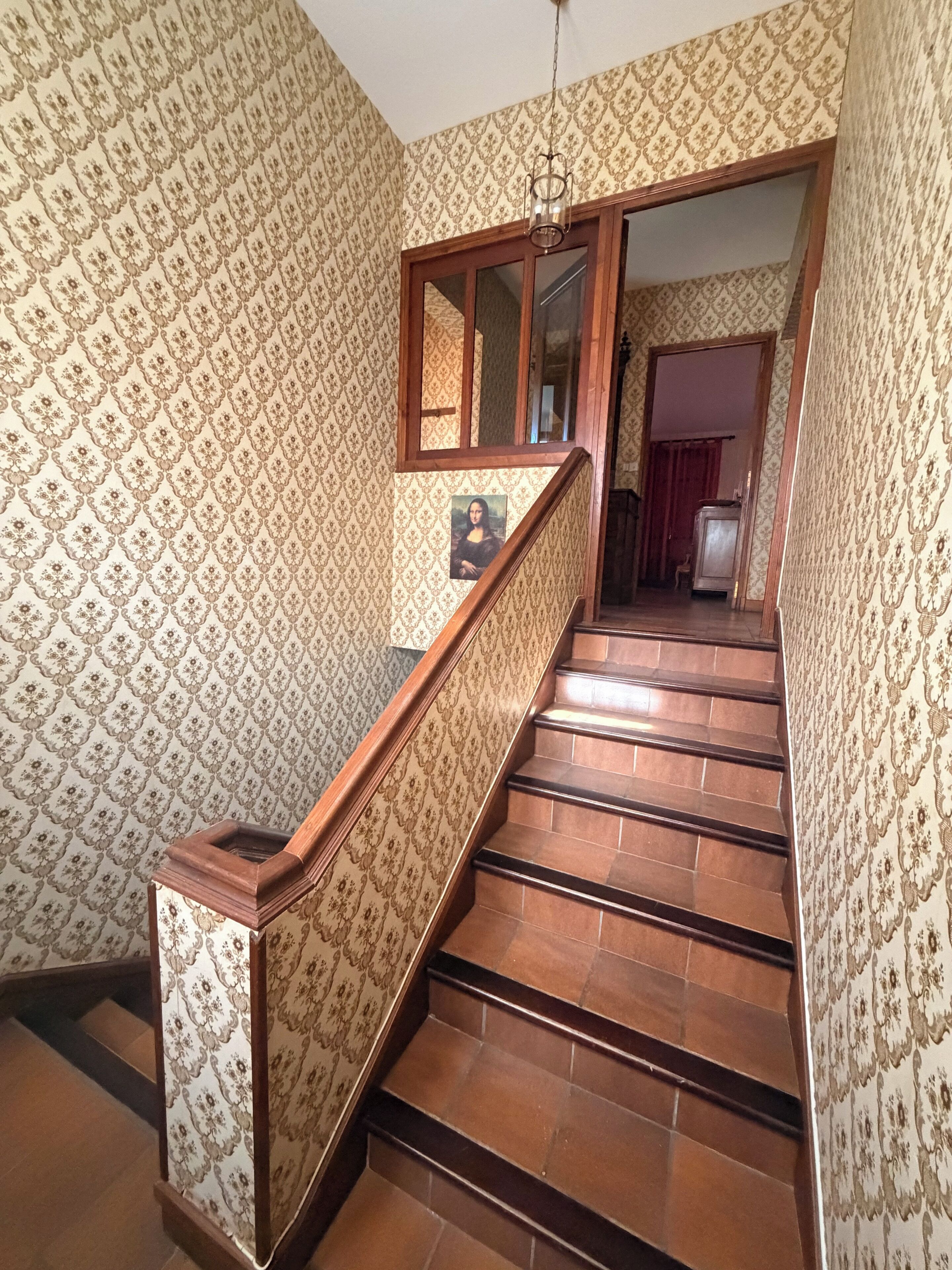 Un escalier avec du papier peint à motifs et une main courante en bois.