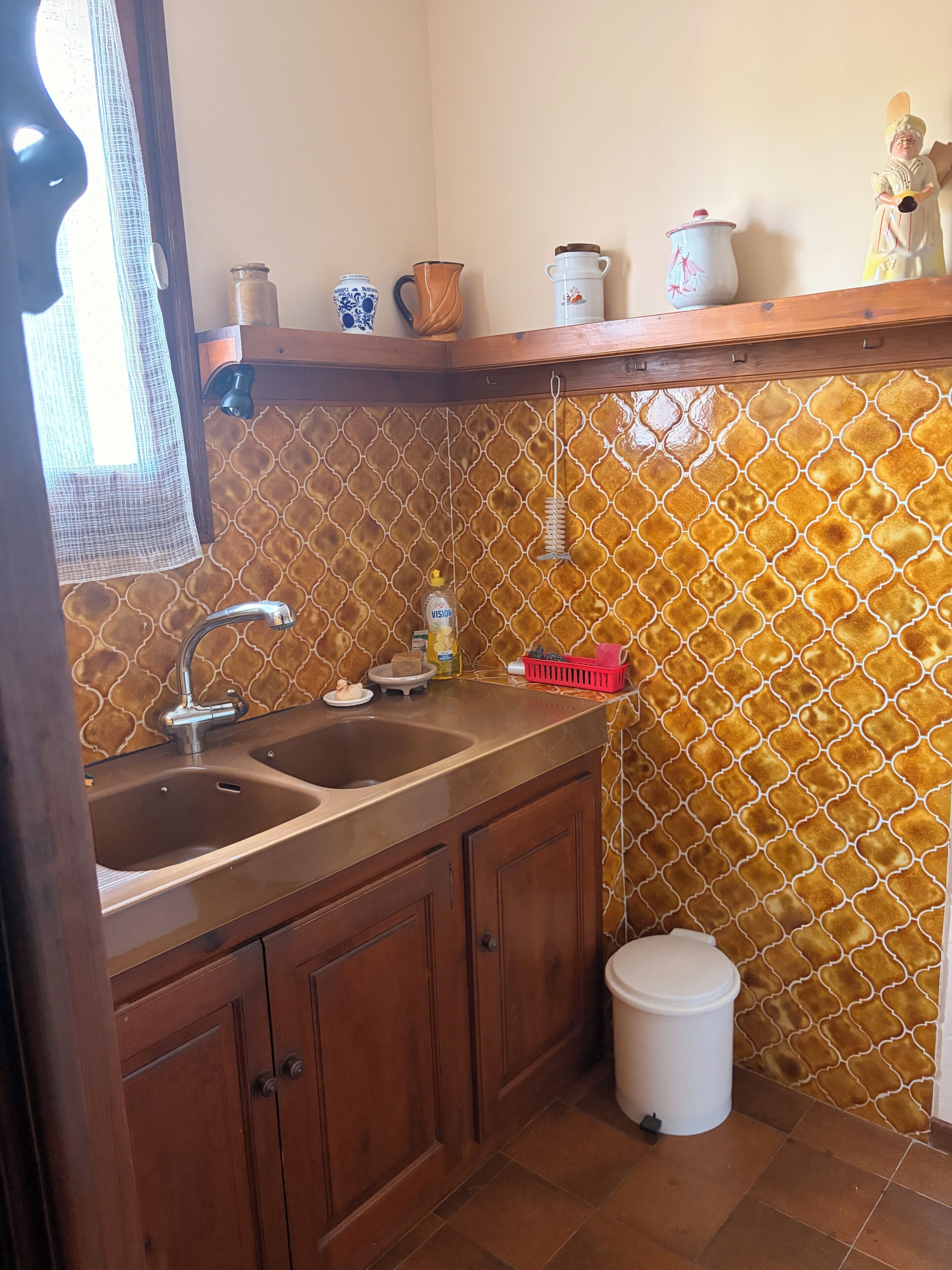 Una cucina con due lavandini, mobili in legno, una lampada a sospensione e uno schienale piastrellato.