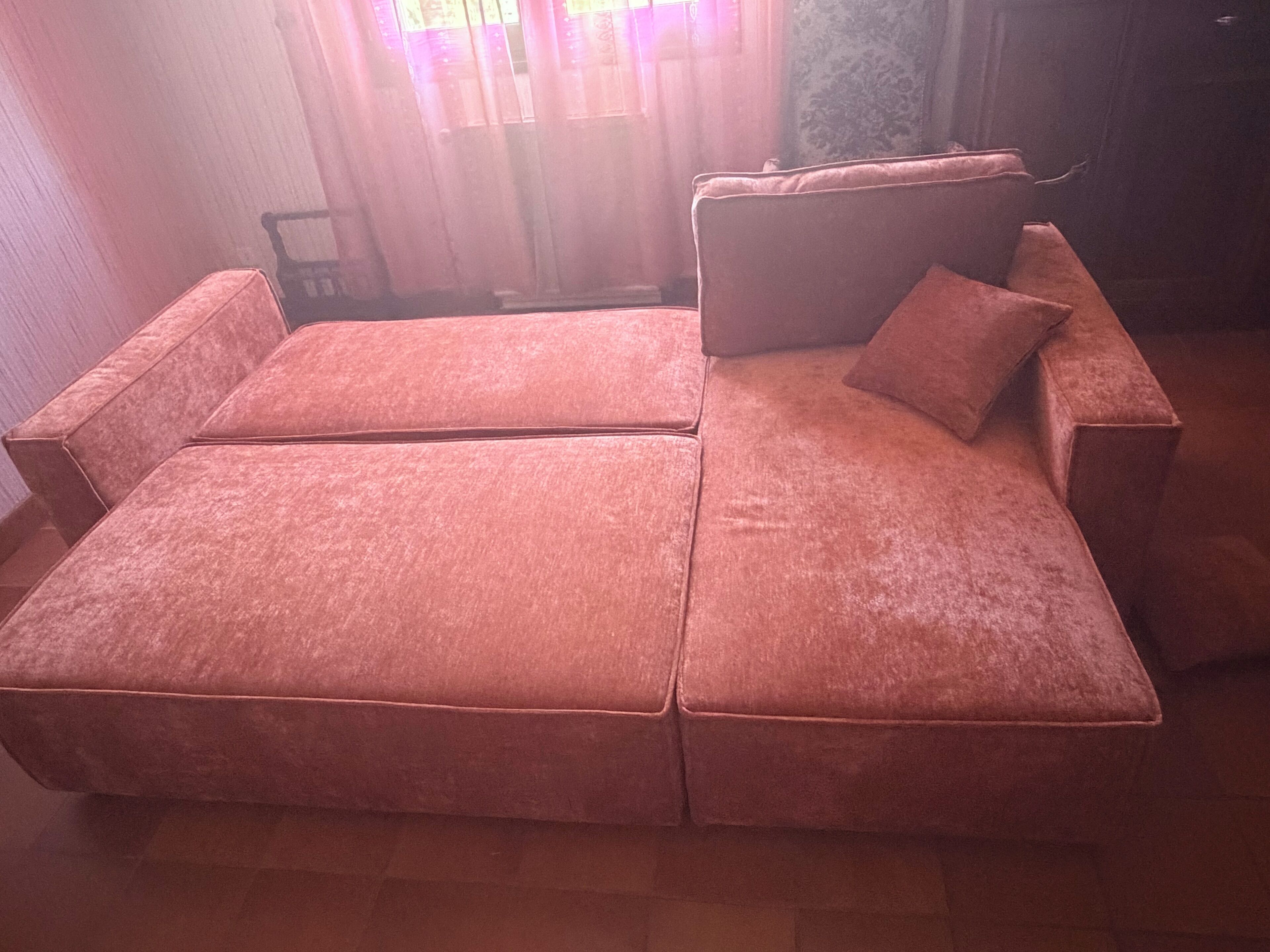 Um sofá modular com chaise longue, uma mesinha e uma janela com cortinas.