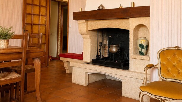 Um quarto com lareira, uma mesa de madeira com cadeiras e um relógio na parede.